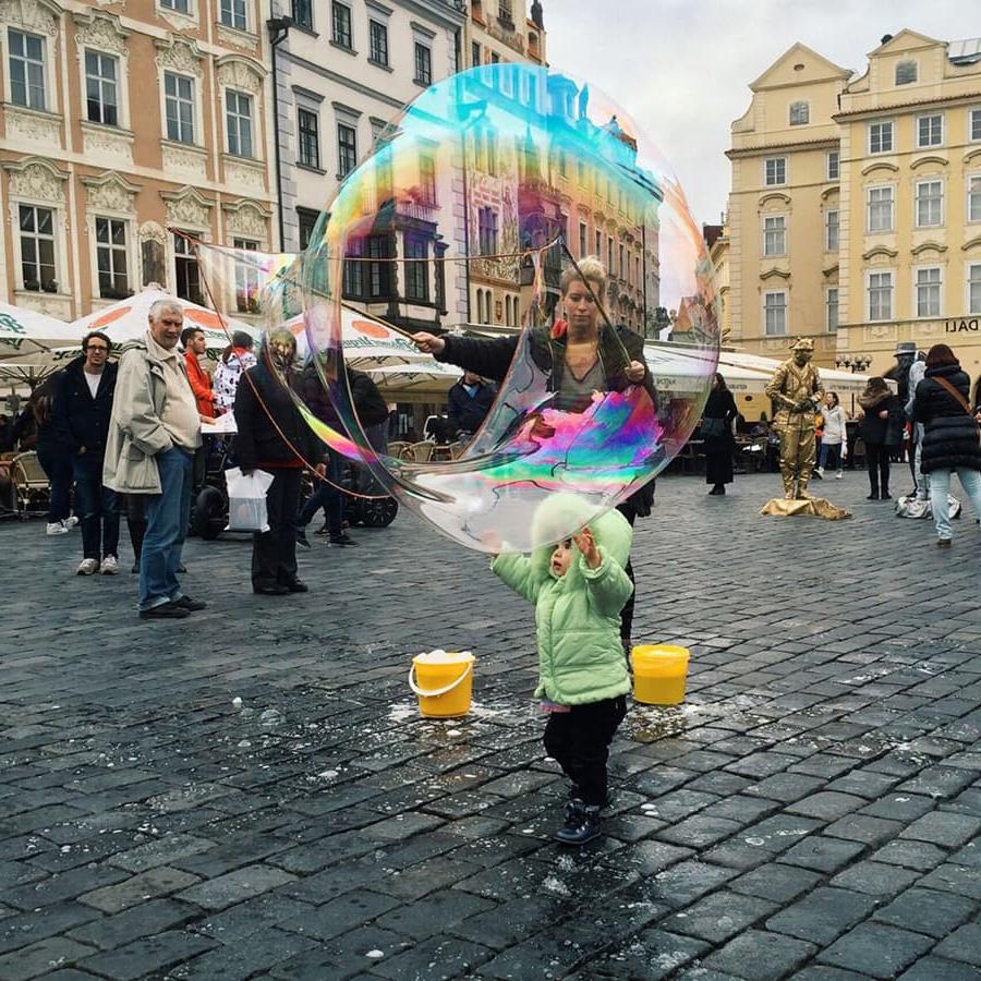 一个孩子在欧洲的广场上吹着巨大的彩虹泡泡